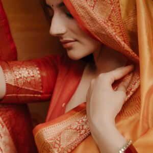 Close-up of a woman wearing an ornate red and orange saree, showcasing intricate design.