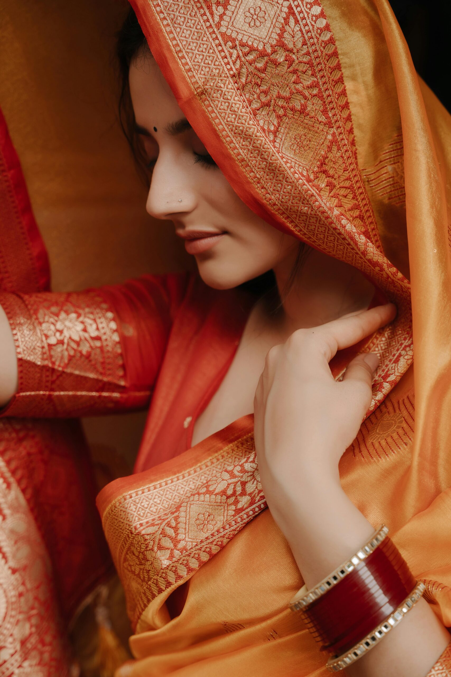 Close-up of a woman wearing an ornate red and orange saree, showcasing intricate design.